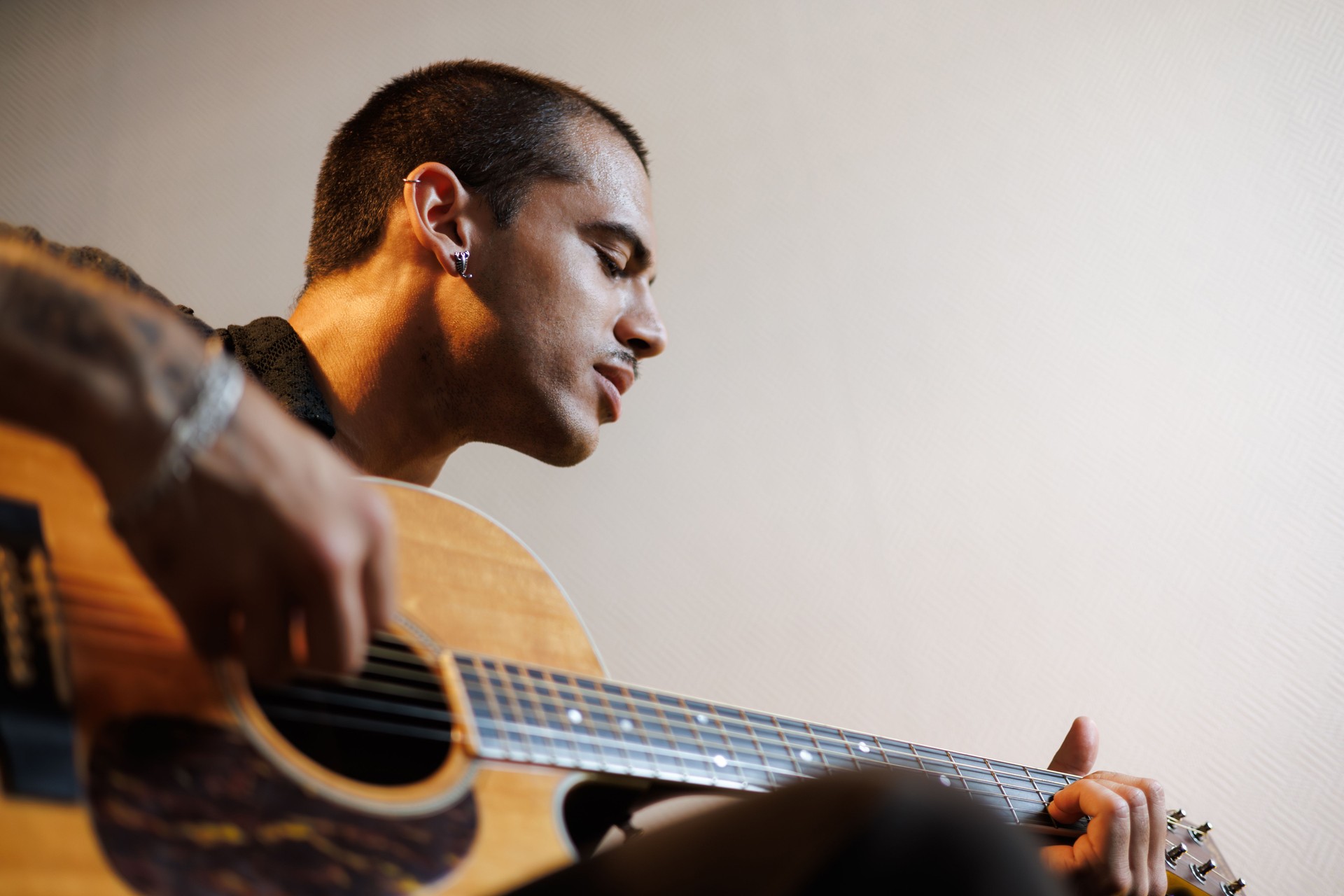 Young musician playing acoustic guitar and singling in music studio